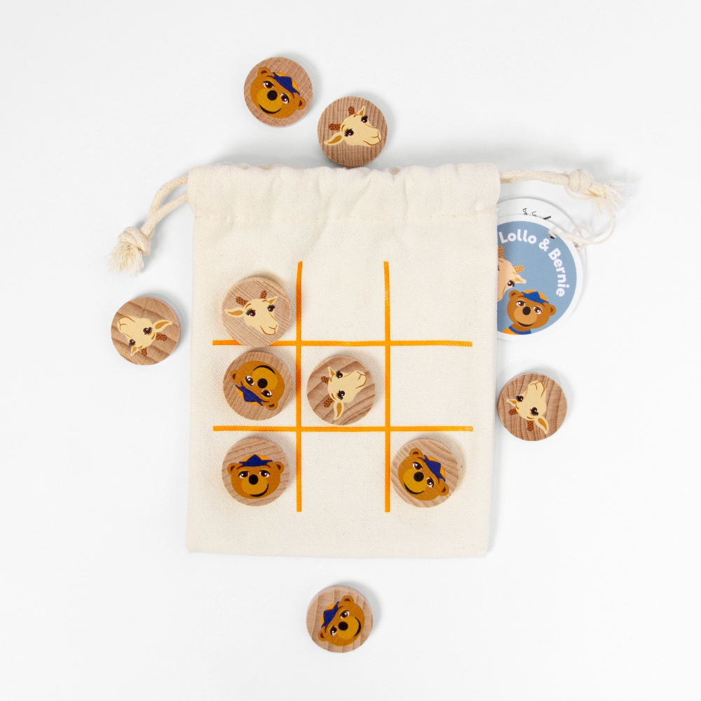 En bild uppifrån på ett portabelt spel Tre i rad med en tygpåse med dragsko och ett orange rutnät, samt spelbrickor i trä dekorerade med ansiktena av giraffen Lollo och björnen Bernie.